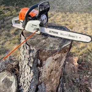 May include: A Stihl Wood Boss chainsaw, featuring an orange and white body with a black handle, rests on a tree stump. The chainsaw's blade is silver, and the text "Stihl Wood Boss" is visible.