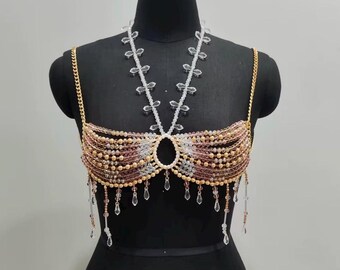 Op de afbeelding: Een met kralen bezette top met een gouden kettingband en een bijpassende ketting. De top heeft een mix van gouden, roze en heldere kralen, met bungelende kristallen accenten. Het kledingstuk wordt getoond op een zwarte mannequin.