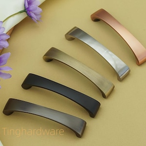 May include: A selection of cabinet handles in different metallic finishes, such as bronze, silver, and copper. The handles have a curved design. The word "Tinghardware" is visible in the image.