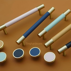 Può includere: Una collezione di ferramenta per mobili, tra cui diverse maniglie a barra e pomelli rotondi. Le maniglie hanno estremità color ottone e sono disponibili in vari colori, tra cui rosa, blu navy, azzurro e beige. I pomelli hanno schemi di colori coordinati.