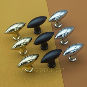 May include: An assortment of cabinet knobs in gold, silver, and black. The knobs have an oval shape and are mounted on a round base. The text "Ting hardware" is visible on the bottom of the image.