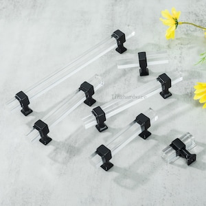 Könnte beinhalten: Eine Sammlung klarer Acryl-Schrankgriffe mit schwarzen Metallsockeln. Die Griffe sind rechteckig und in verschiedenen Größen erhältlich. Der Text "Tinghardware" ist im Bild enthalten.