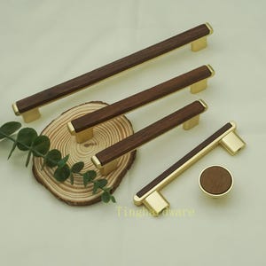 Op de afbeelding: Een verzameling houten kastgrepen en een knop met messingkleurige accenten. De grepen zijn rechthoekig met een donkerbruin houten middenstuk en messingkleurige uiteinden. De knop is rond met een bijpassend houten middenstuk. De tekst "Tinghardware" is zichtbaar.