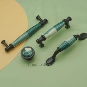 Może przedstawiać: Zestaw okuć do szafek z zielono-białym wzorem w kratę na uchwytach i gałce. Okucia mają ciemne brązowe wykończenie. Zestaw zawiera dwa uchwyty, gałkę i uchwyt w kształcie łyżki.