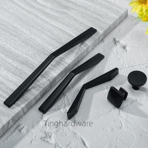 Op de afbeelding: Een collectie zwarte kastbeslagen, waaronder handgrepen en knoppen. De set heeft verschillende vormen en maten, met een matte afwerking. De hardware wordt gepresenteerd op een lichtgrijze ondergrond, wat een modern design laat zien.