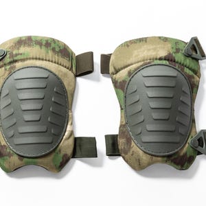 May include: A pair of camouflage knee pads. Each pad features a hard, dark gray plastic shield with horizontal ridges, surrounded by a camouflage fabric in shades of green, brown, and tan. Adjustable straps and buckles are visible.