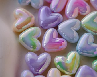 May include: A collection of iridescent heart-shaped beads in various pastel colors, including pink, purple, blue, and yellow. The beads have a glossy finish and reflect light, creating a shimmering effect. These decorative beads are ideal for crafting and jewelry making.