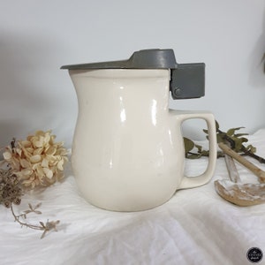 May include: A white ceramic jug with a grey lid and handle. The lid has a latch that can be used to secure it.
