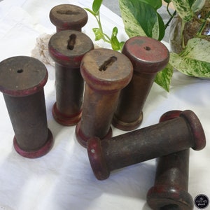 May include: A collection of vintage wooden spools with a dark brown finish and red accents. The spools have a cylindrical shape with a keyhole-shaped opening on top. The spools are arranged on a white surface.
