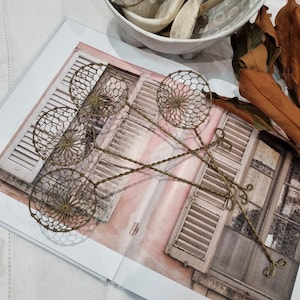 May include: Three antique-style brass wire strainers with circular mesh bowls and long, twisted wire handles. Each strainer features a fine hexagonal wire mesh pattern and a looped end on the handle, crafted from metallic brass-toned wire material.