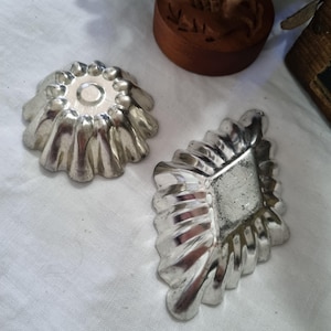 May include: Two silver metal cake moulds. One is round with a fluted edge and the other is diamond shaped with a fluted edge.