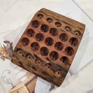 May include: A rectangular wooden organiser block featuring a natural brown grain and multiple circular recessed holes of varying sizes arranged in a grid pattern, designed for holding small cylindrical items in an upright position.