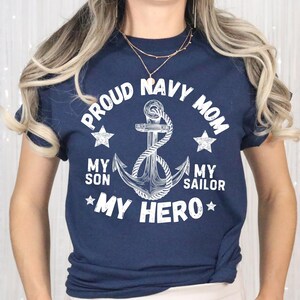 May include: Navy blue t-shirt with white text and a nautical anchor design. The text reads "PROUD NAVY MOM" above the anchor, with "MY SON MY SAILOR MY HERO" below. Two stars flank the anchor.