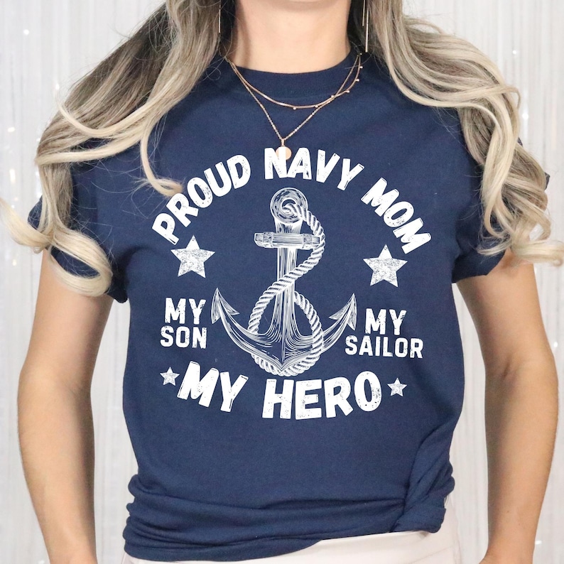 May include: Navy blue t-shirt with white text and a nautical anchor design. The text reads "PROUD NAVY MOM" above the anchor, with "MY SON MY SAILOR MY HERO" below. Two stars flank the anchor.