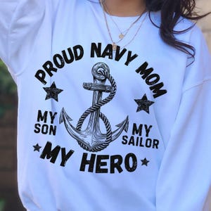 May include: White sweatshirt with the text "PROUD NAVY MOM" in a circular design around a black and white anchor graphic. The text "MY SON MY SAILOR MY HERO" is also included, along with star graphics.