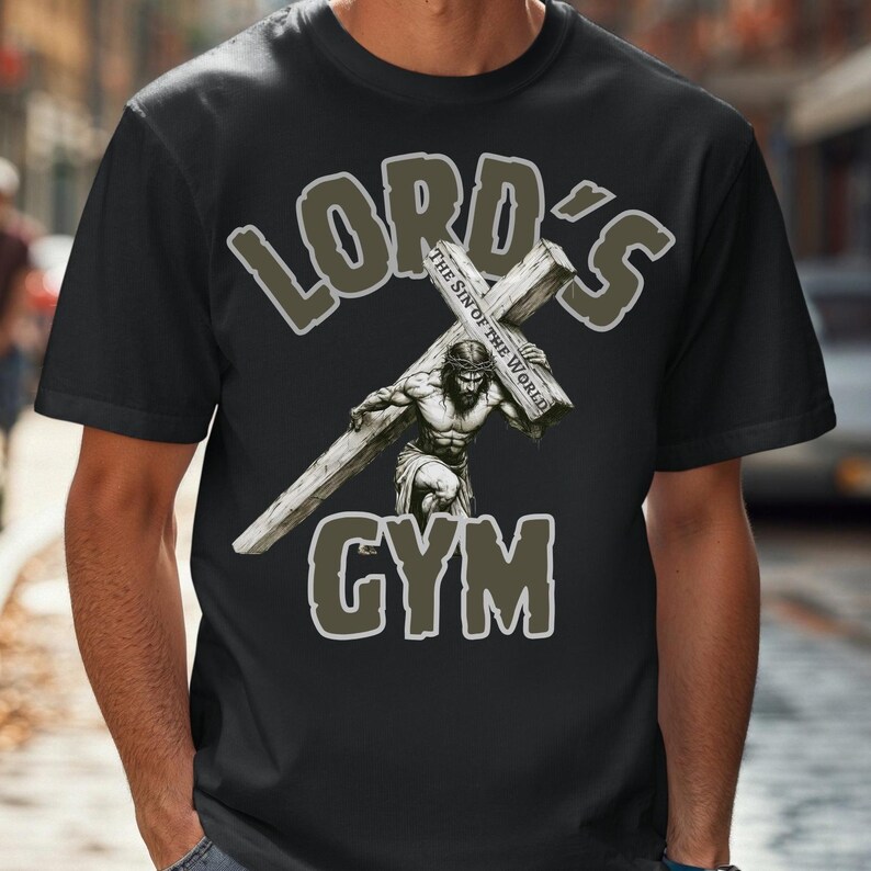 Puede incluir: Camiseta negra con un dise&ntilde;o gr&aacute;fico que presenta una figura musculosa que lleva una cruz. El texto "LORD'S GYM" est&aacute; encima y debajo de la imagen, con "THE SIN OF THE WORLD" en la cruz. El dise&ntilde;o es en tonos grises y blancos.