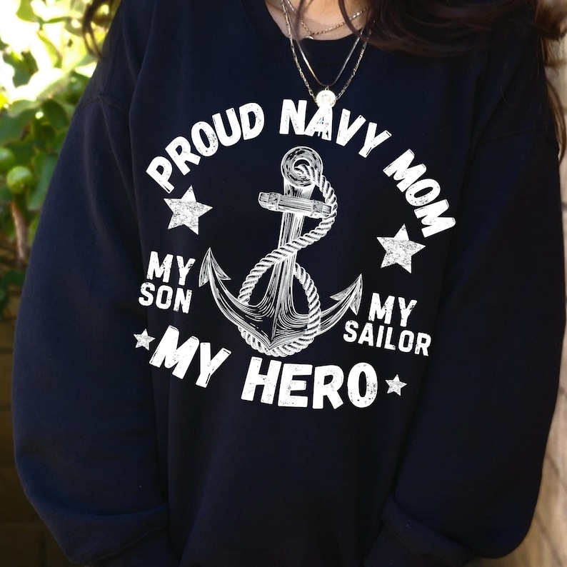 May include: Navy blue sweatshirt with a white anchor design and the text "PROUD NAVY MOM." The design includes stars and the phrases "MY SON," "MY SAILOR," and "MY HERO."