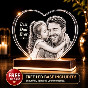 May include: A heart-shaped clear acrylic plaque featuring a black and white photograph of a child hugging a man. The text 'Best Dad Ever' is engraved on the left side. The plaque is mounted on a rectangular wooden base with integrated LED lighting.