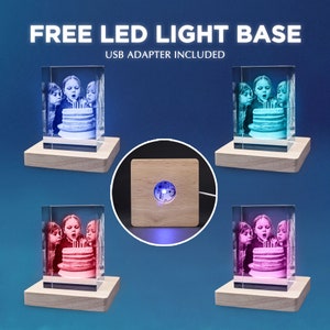 Puede incluir: Cuatro bloques de vidrio rectangulares con una imagen grabada en l&aacute;ser 3D de ni&ntilde;os soplando velas de cumplea&ntilde;os, sobre una base LED de madera clara. El texto dice FREE LED LIGHT BASE y USB ADAPTER INCLUDED. Se muestra una base por separado.