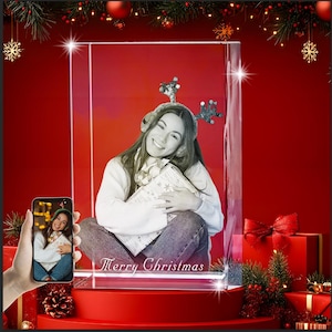 Puede incluir: Un bloque de vidrio rectangular con una fotograf&iacute;a en blanco y negro grabada con l&aacute;ser de una persona que lleva astas de reno y un su&eacute;ter, sosteniendo un regalo. La base del bloque de vidrio muestra el texto grabado Merry Christmas.