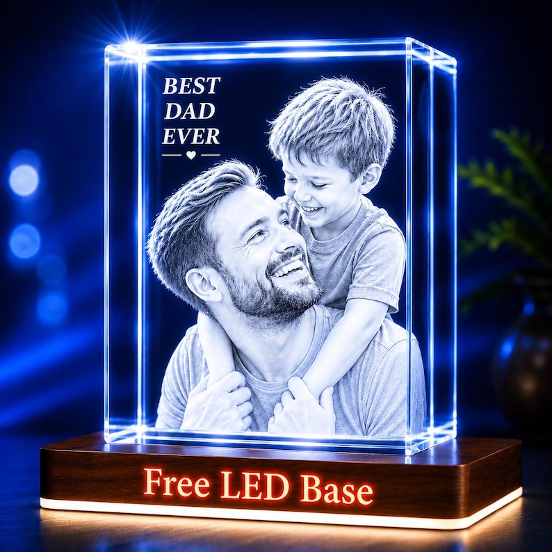 Puede incluir: Un bloque de vidrio rectangular con una fotograf&iacute;a en blanco y negro grabada con l&aacute;ser de un hombre y un ni&ntilde;o abrazados. El texto BEST DAD EVER est&aacute; grabado encima. El vidrio descansa sobre una base de madera oscura con el texto Free LED Base.