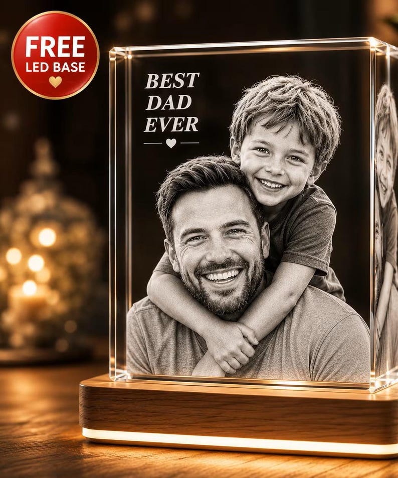 Puede incluir: Un bloque de vidrio rectangular con una fotograf&iacute;a grabada con l&aacute;ser en blanco y negro de un adulto y un ni&ntilde;o sonrientes abrazados. El texto BEST DAD EVER est&aacute; grabado sobre las figuras. El vidrio descansa sobre una base de madera LED.