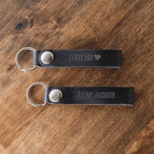 May include: Two black leather keychains with silver key rings. The top keychain has the text "I love you" with a small heart symbol. The bottom keychain has the text "Jeremy Jackson".