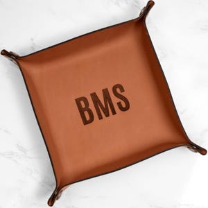 May include: A brown leather tray with a monogrammed design. The initials "BMS" are embossed in the center of the tray.