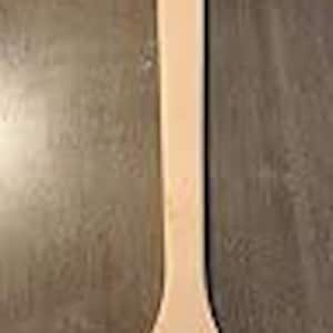 May include: A light-colored wooden spoon with a long handle and a rounded bowl. A small hole is drilled at the top of the handle, with a natural-colored string attached for hanging. The spoon is made of a light-colored wood.