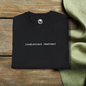 May include: Black t-shirt with the text "(indistinct chatter)" printed in white on the front.