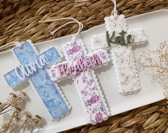 May include: Three white wooden crosses with scalloped edges, each decorated with a different floral pattern. The crosses are personalized with the names "Olivia", "Elizabeth", and "Kate" in different colors.