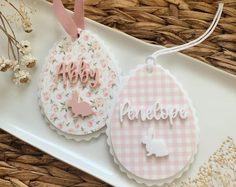 May include: Two pink and white Easter egg-shaped ornaments with bunny silhouettes and personalized names, Abby and Penelope.