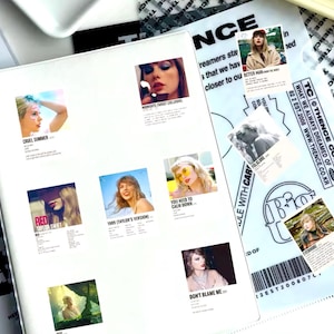 May include: A white sheet of paper with several colorful square stickers featuring album covers by Taylor Swift. The stickers feature album titles like "Cruel Summer", "Red", "You Need to Calm Down", "1989 (Taylor's Version)", "Don't Blame Me", "Folklore", "Evermore", and "Better Man".