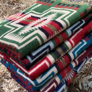 May include: A stack of five colorful woven blankets with geometric patterns. The blankets are folded and stacked on top of each other, with the top blanket being green and white. The blankets are made of a soft, comfortable material and are perfect for keeping warm on a cold day.