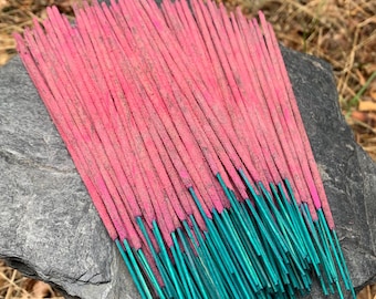 May include: A bundle of pink and teal incense sticks on a gray stone. The sticks are arranged in a neat pile.