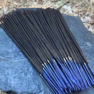 Puede incluir: Un paquete de varillas de incienso negras con puntas azules, dispuestas sobre una superficie de piedra gris.