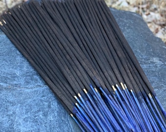 May include: A bundle of black incense sticks with blue tips, arranged on a grey stone surface.