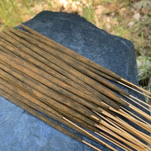 May include: A bundle of brown incense sticks with a light brown coating on a gray stone surface.