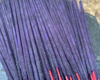 May include: A close-up of a bundle of incense sticks. The top of the sticks are a deep purple, fading into a bright red at the base. The incense sticks are tightly packed together, creating a textured appearance.