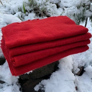 May include: A stack of four red wool blankets folded neatly on top of a pile of rocks covered in snow.