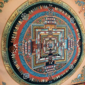 May include: A colorful mandala with intricate details and gold accents. The mandala is surrounded by a black circle with gold lettering. The background is a light peach color.