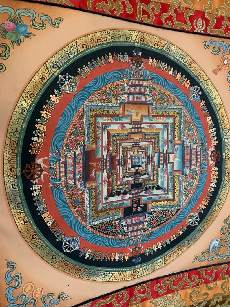 May include: A colorful mandala with intricate details and gold accents. The mandala is surrounded by a black circle with gold lettering. The background is a light peach color.