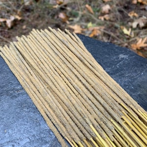 May include: A bundle of brown incense sticks with a light brown base. The sticks are arranged in a neat row on a dark gray surface.