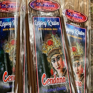 May include: Three packages of incense sticks with a colorful label featuring a woman in traditional Balinese clothing. The label reads "Legong Kraton Dupa Herbal Bali Cendana Premium Quality" and lists features like "100 Natural" and "Abu Tidak Panas".