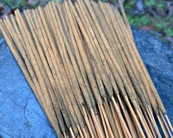 Peut inclure: Gros plan sur un ensemble de bâtonnets d'encens de couleur brun clair avec des extrémités foncées. Les bâtonnets sont disposés en rangées serrées, sur un fond flou de feuillage vert et une surface de pierre bleue.