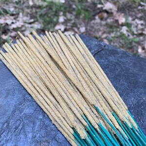 May include: A bundle of incense sticks with a light brown color and a green base. The sticks are arranged in a fan shape.