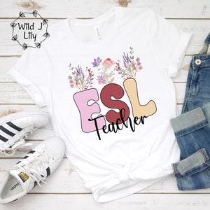 Może przedstawiać: Biała koszulka z napisem "ESL Teacher" w kolorowych literach z kwiatowym wzorem nad tekstem.