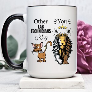 Puede incluir: Taza de cerámica blanca con asa negra. La taza tiene un gráfico de un león con una corona y un gato con un parche en el ojo y una venda en la cola. El texto en la taza dice "Other Lab Technicians" con flechas apuntando hacia abajo y "You" con estrellas sobre el león.