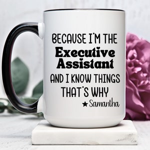 Puede incluir: Taza de café de cerámica blanca con asa negra y borde negro. La taza tiene texto negro que dice "Because I'm the Executive Assistant and I know things that's why *Samantha".