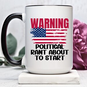 May include: White ceramic coffee mug with a black handle and rim. The mug has a distressed American flag design with the text "WARNING POLITICAL RANT ABOUT TO START" in black.